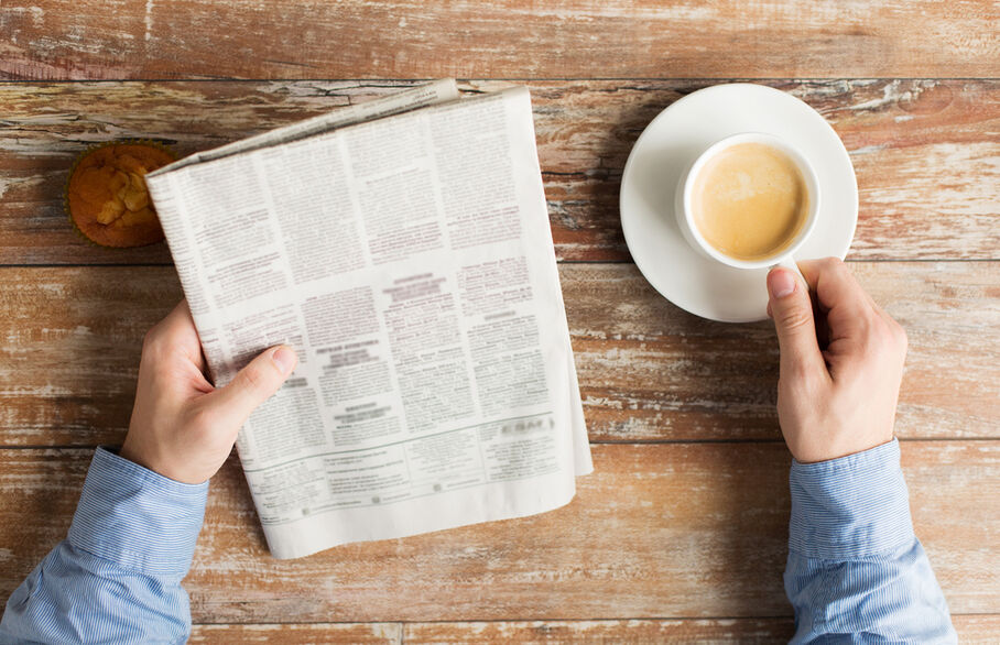 Someone reading a newspaper and holding a cup of coffee