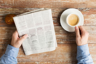 Someone reading a newspaper and holding a cup of coffee