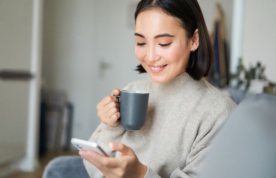 A person looking at a phone while holding a mug