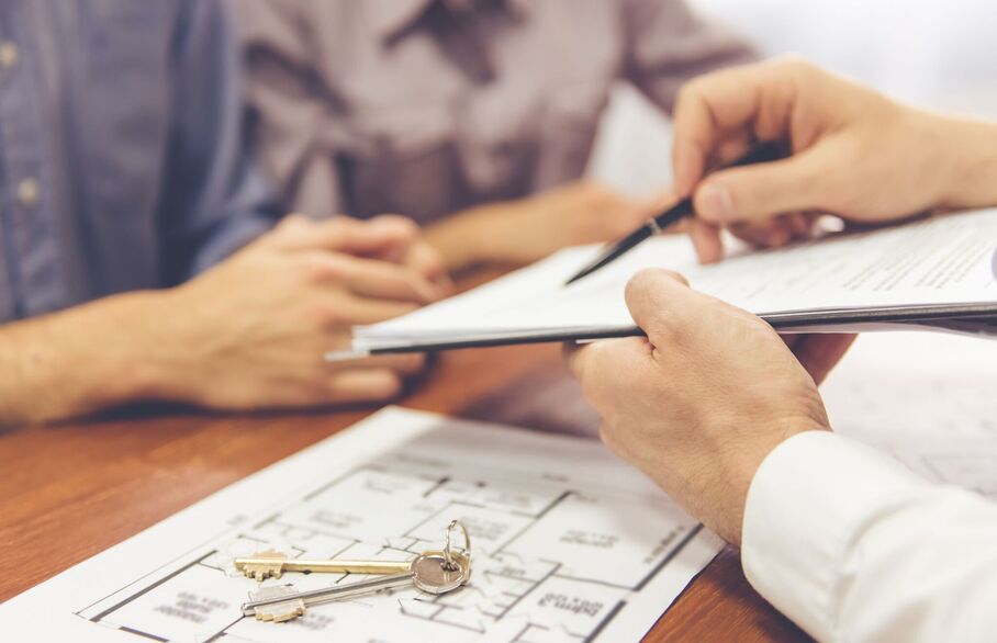 Someone pointing at a clipboard with a house floorplan and pair of keys beneath