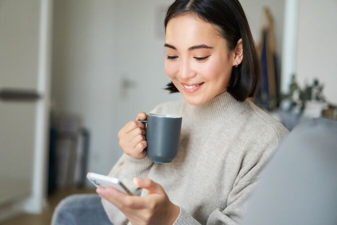 A person looking at a phone while holding a mug