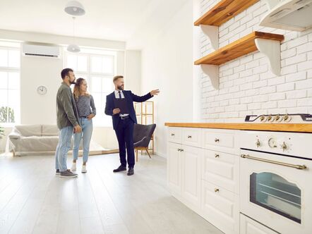 A young couple being shown around a kitchen by an estate agent