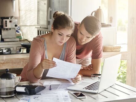 A young couple looking at a piece of paper in front of a laptop